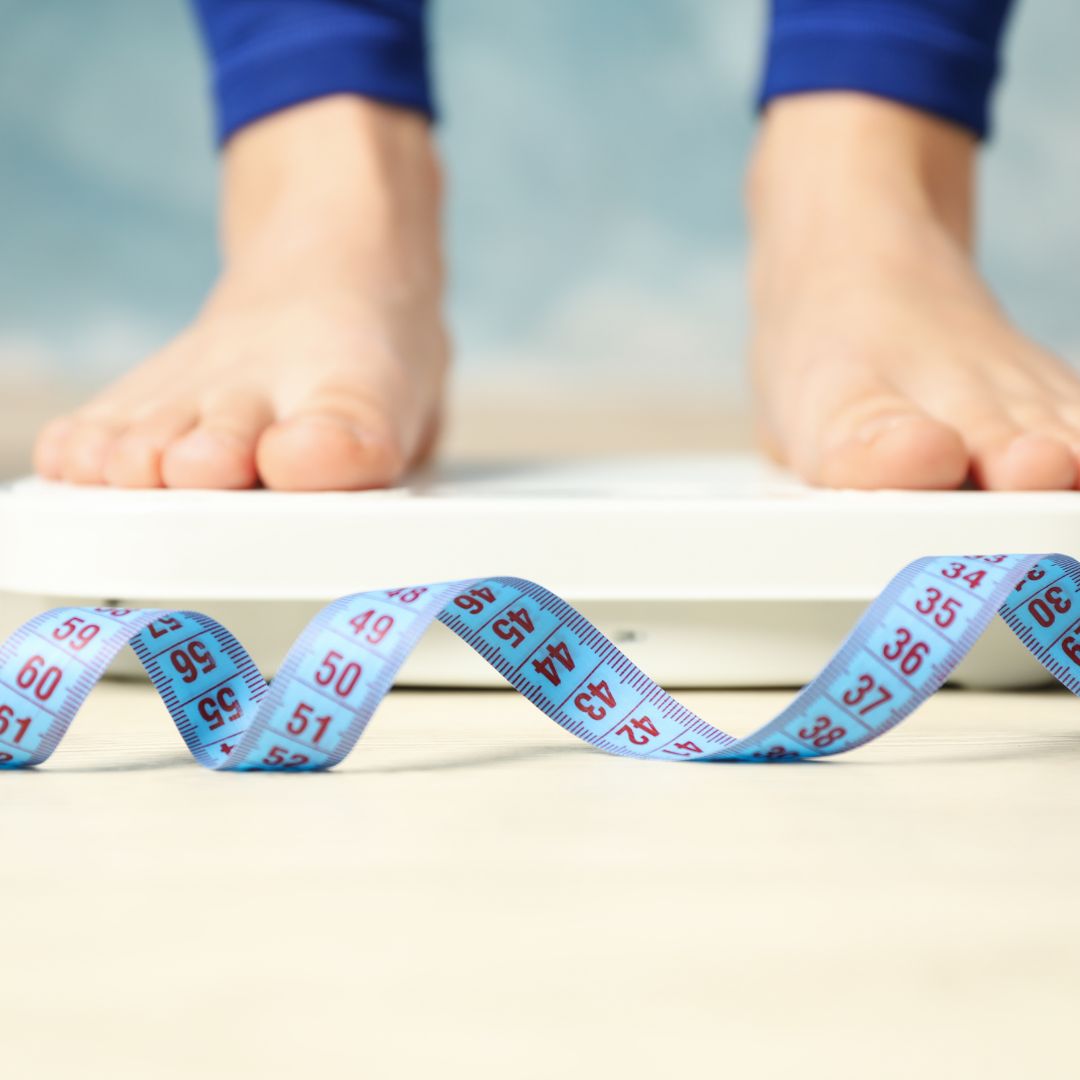 woman standing on a scale next to a tape measure